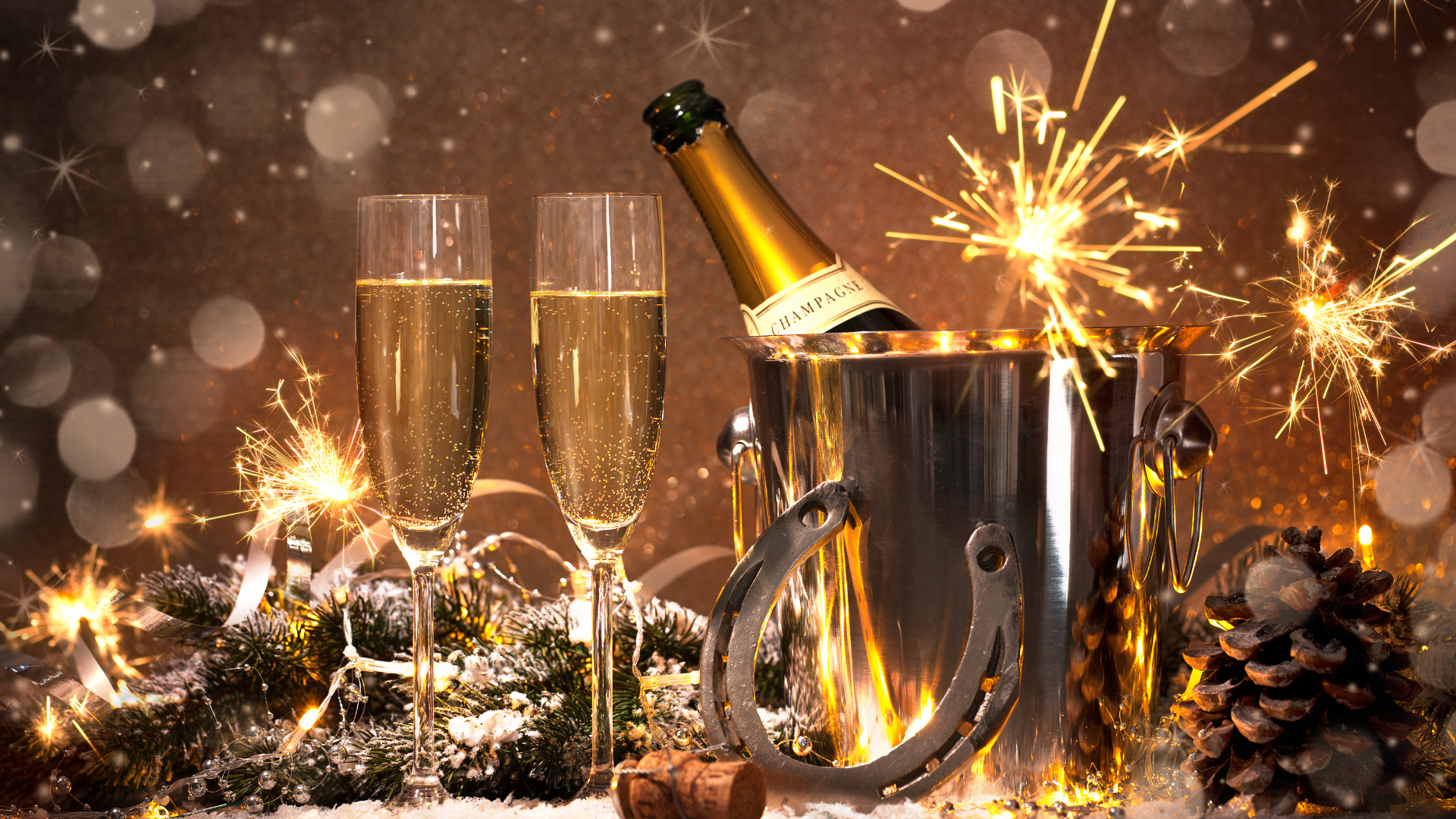 Champagne flutes with sparklers, bottle in ice bucket; festive holiday celebration with pinecones and bokeh lights.