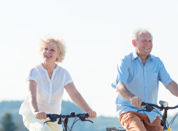 Elderly couple joyfully cycling outdoors on a sunny day, embracing an active lifestyle and nature.